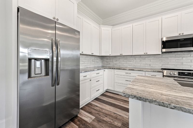 Stainless steel refrigerator next to white kitchen cabinets and countertop with microwave.