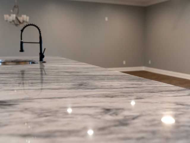 Close-up of a polished, marble-patterned countertop with a black faucet, and a light gray wall in the background.