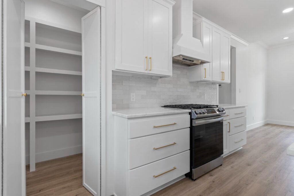 White kitchen with cabinets, oven, and pantry; wood floors.