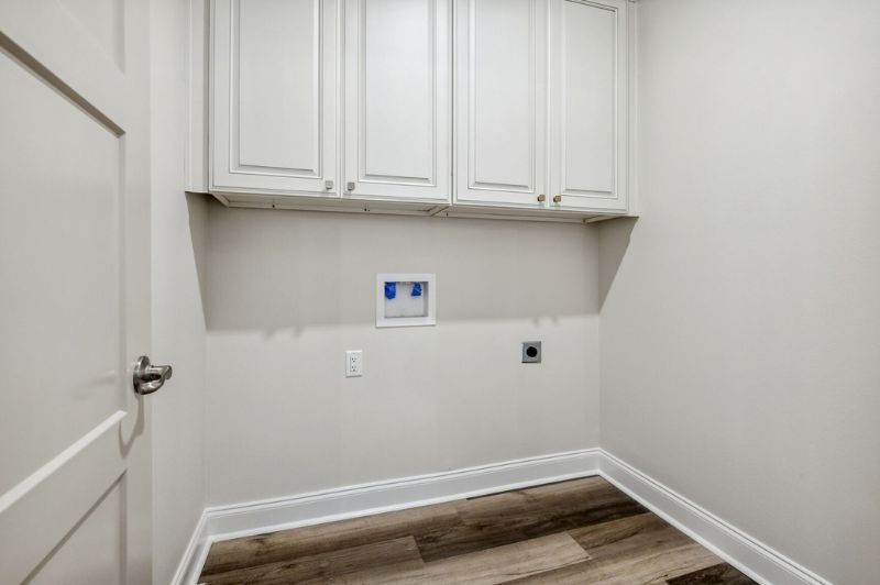 Small, white laundry room with upper cabinets, water hookups, and wood-look floor.