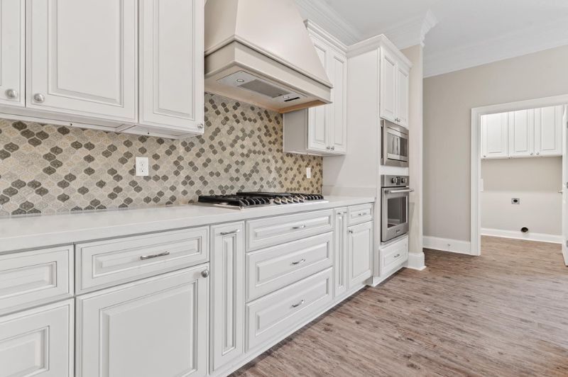 White kitchen with light-colored cabinetry, gas cooktop, mosaic tile backsplash, and stainless steel appliances.