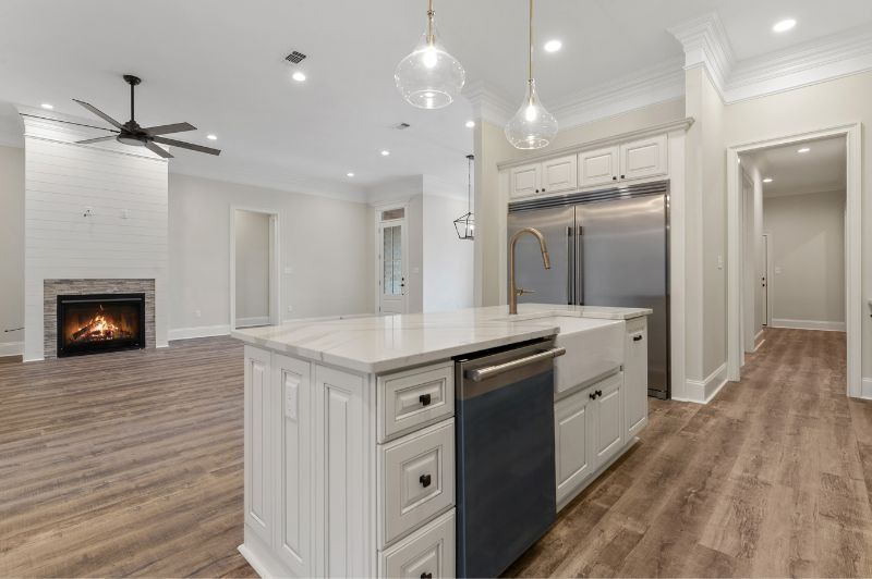 Spacious, bright kitchen with white cabinets, island, and stainless steel appliances, opening to a living area with a fireplace.