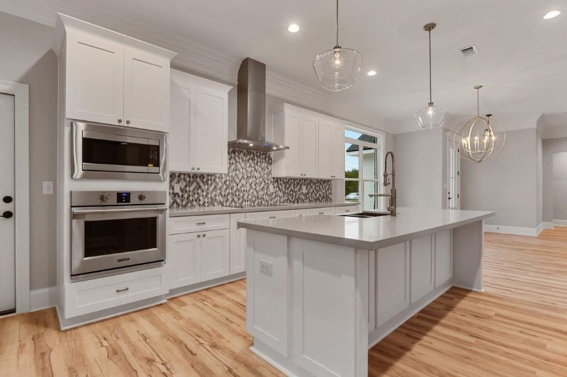 Modern white kitchen with stainless steel appliances, island, and wood flooring.