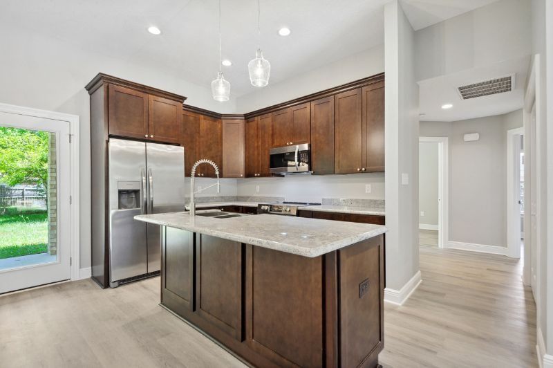 Modern kitchen with dark cabinets, stainless steel appliances, and light wood floors.