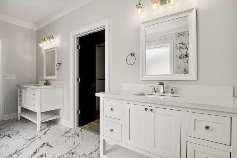 Two white vanities in a modern bathroom with marble flooring and a black doorway.
