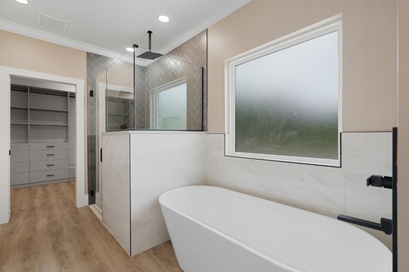 Modern bathroom with a tub, shower, and walk-in closet; neutral tones and natural light.