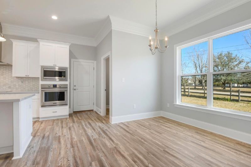 Bright kitchen/dining area with white cabinets, light gray walls, wooden floors, and large window.