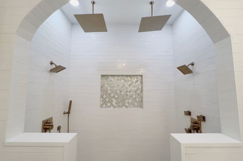 A bright white, tiled shower with two rain shower heads, two side shower heads, and a decorative tile inset.