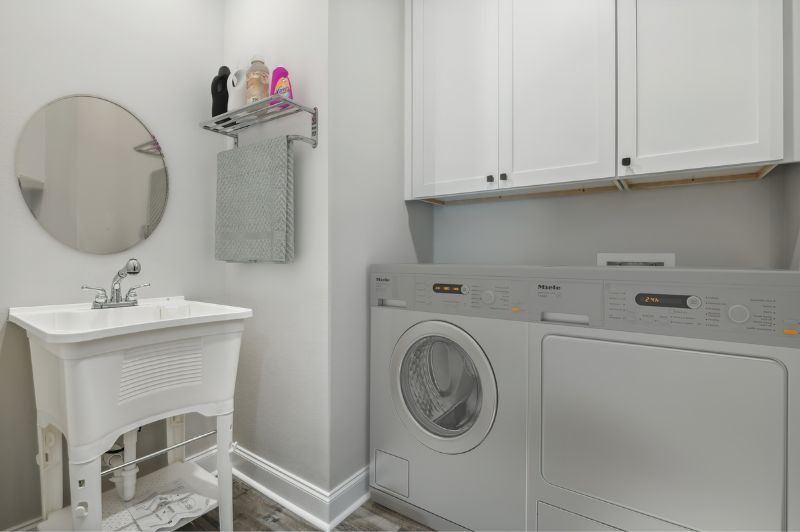 Laundry room with a washer, dryer, sink, and cabinets; white and gray color scheme.