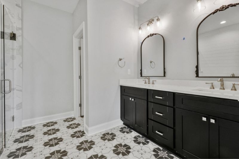 Bathroom with black cabinets, white countertops, floral floor tile, and arched mirrors.