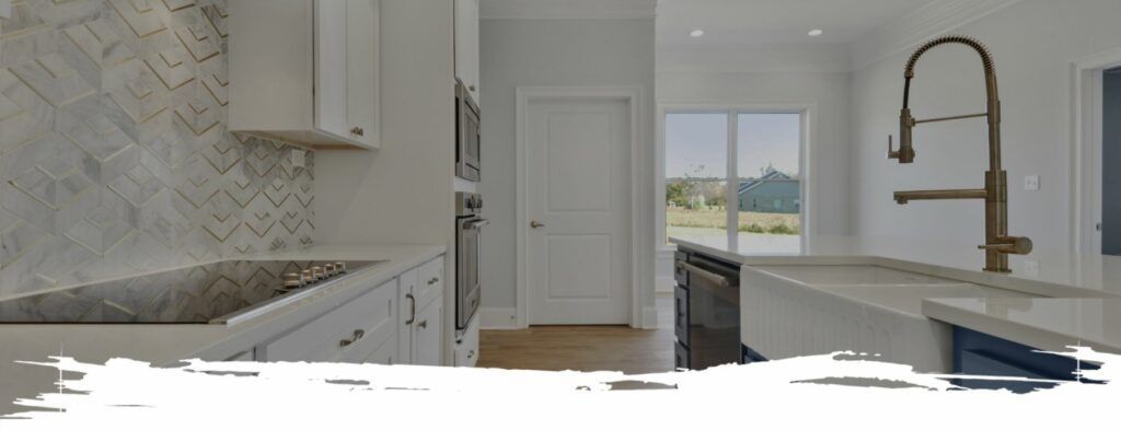 A bright white kitchen with a gold faucet and a view of a window and a door.