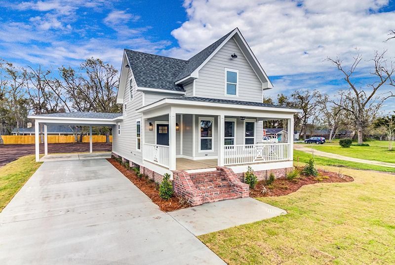 Gray two-story house with a porch, carport, and red brick steps on a sunny day.