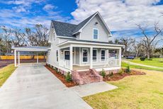 Gray house with covered porch, carport, and green lawn. Sunny day.