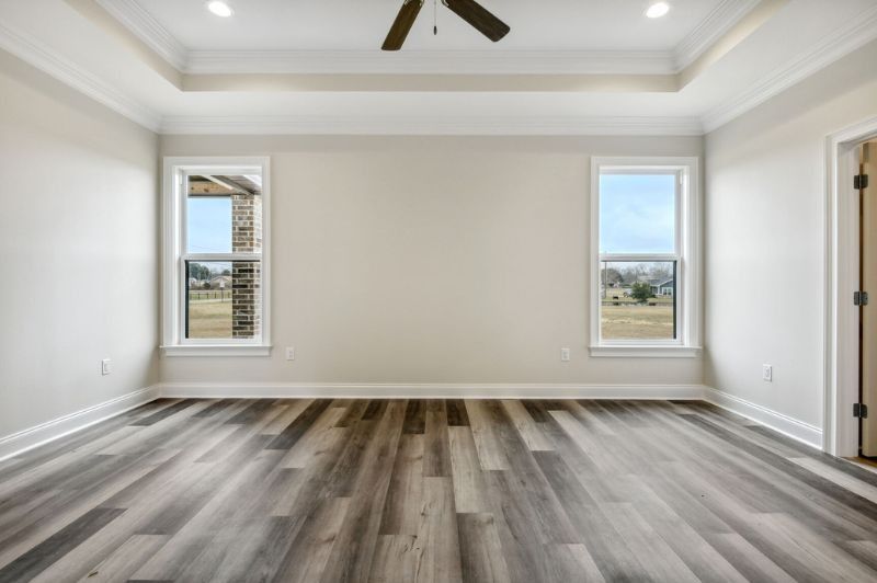 Empty bedroom with wood-look floor, two windows, and white walls, light fixtures and ceiling fan.