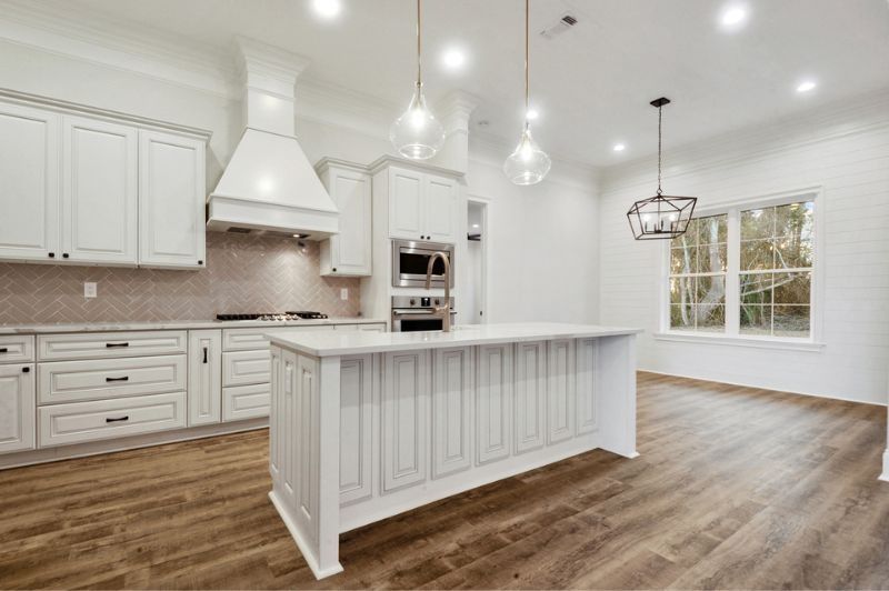 White kitchen with island, cabinets, stove, and wood floors. Windows on the right.