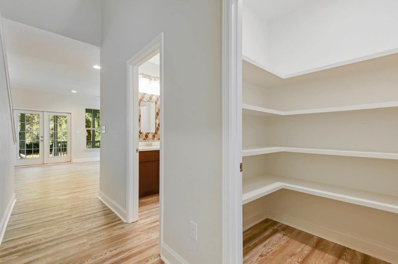 Hallway with pantry and open bathroom doorway, leading to a bright room with patio doors.