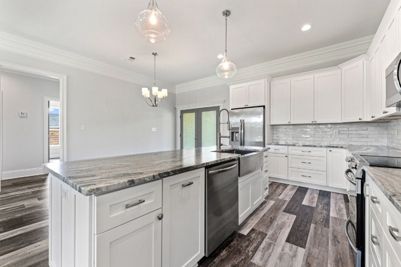 Modern white kitchen with an island, stainless steel appliances, and gray flooring.