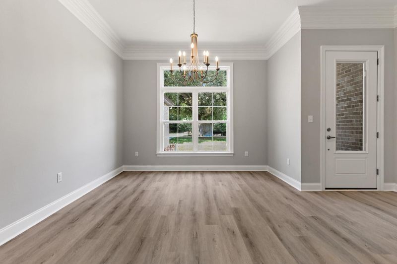 Empty dining room with wood flooring, large window, chandelier, and white trim.