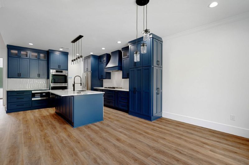 Modern kitchen with navy blue cabinets, white countertops, and wood flooring.