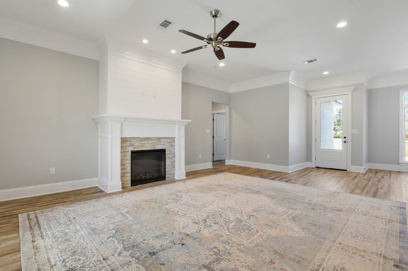 Spacious living room with fireplace, wood floors, and large rug. Gray walls, white trim, and ceiling fan.