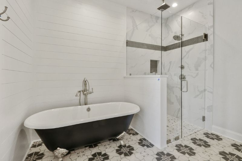 Bathroom with a black claw-foot tub, glass shower, white and gray accents, and patterned floor tiles.