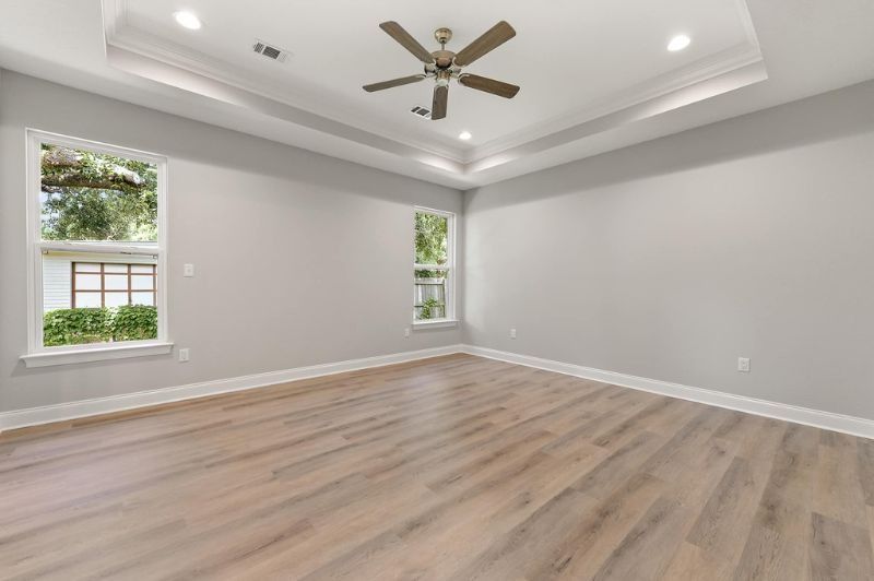 Empty room with light gray walls, wood-look flooring, two windows, and a ceiling fan.