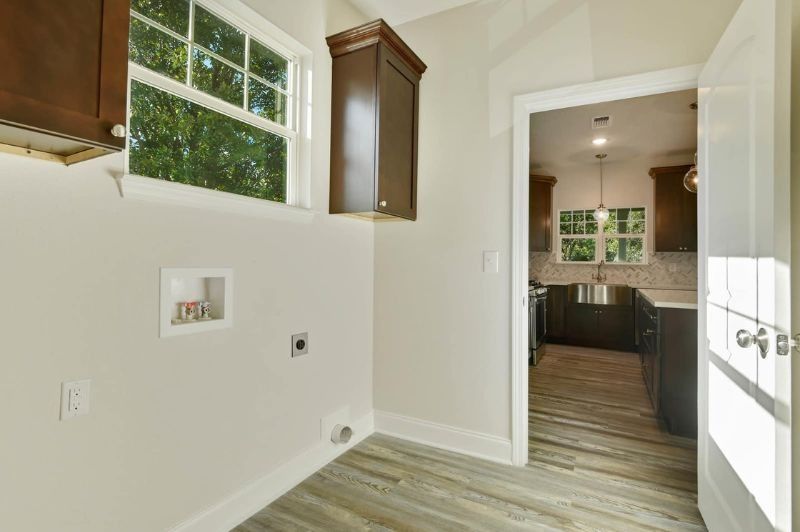 Laundry room with cabinets, window, and doorway to kitchen.