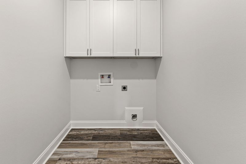 Empty laundry room with overhead white cabinets, washer/dryer hookups, and wood-look flooring.
