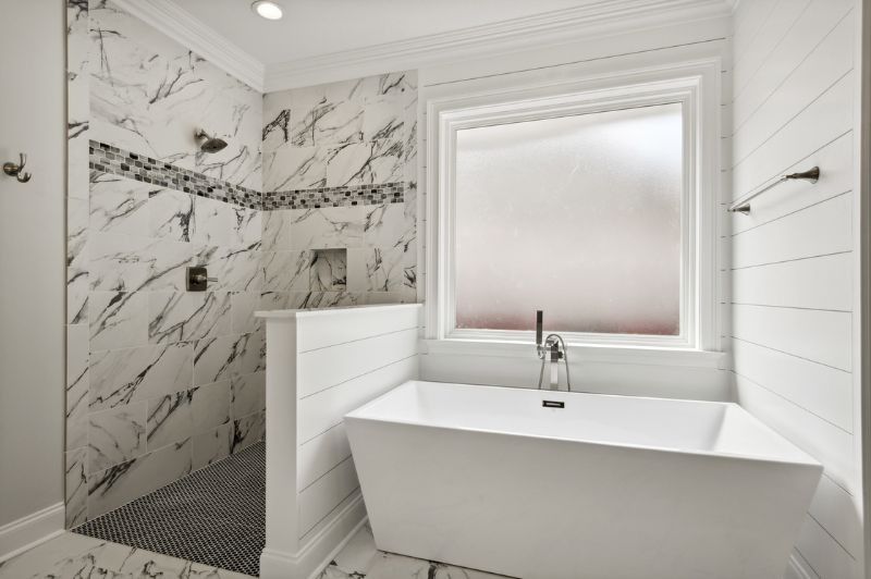 Modern bathroom with marble shower, freestanding tub, and frosted window.