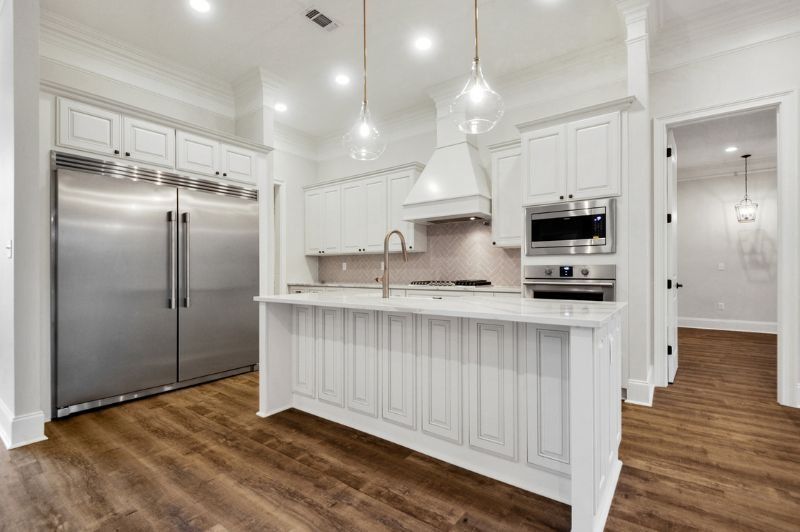 White kitchen with stainless steel refrigerator and island, wood floors.