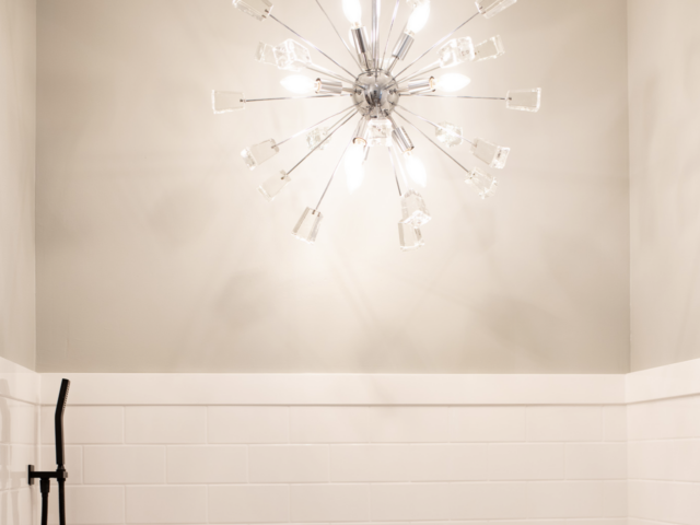 Bright, starburst chandelier in a room with white walls and a black showerhead.