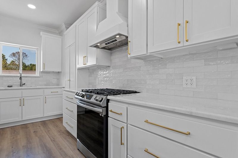 White modern kitchen with gold hardware. Stove, white cabinets, and tiled backsplash.