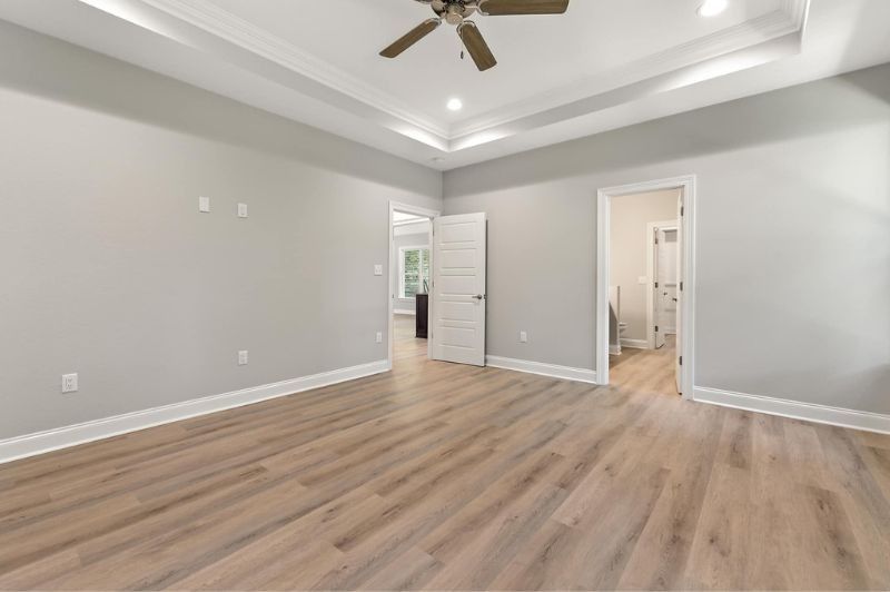Empty bedroom with wood floors, gray walls, white trim and ceiling, and two open doorways.