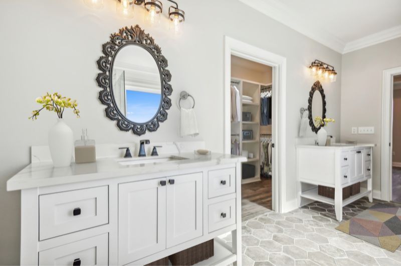 White bathroom with marble vanity, decorative mirror, and walk-in closet entrance.
