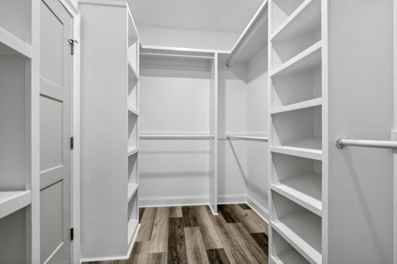 Walk-in closet with white shelves, hanging rods, and a gray-brown wood-look floor.