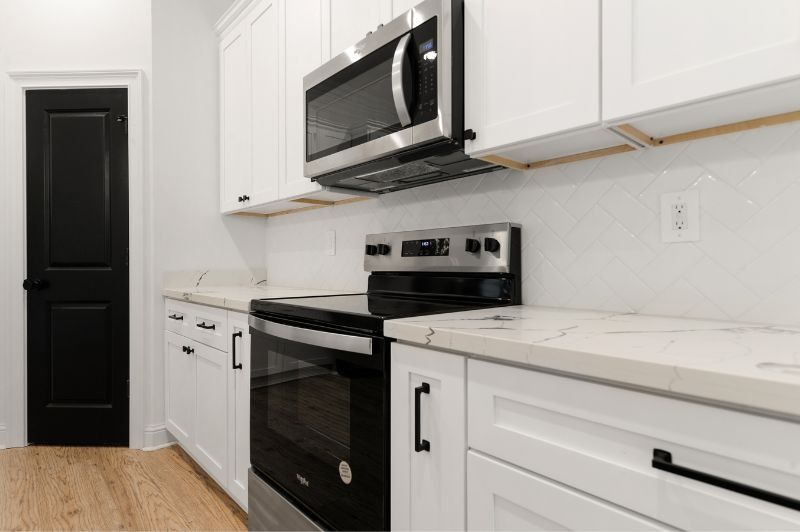 Modern kitchen with white cabinets, black appliances, black door, and light countertops.