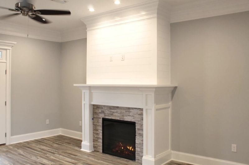 Fireplace with white mantel and stone surround, grey walls, and wood-look flooring.