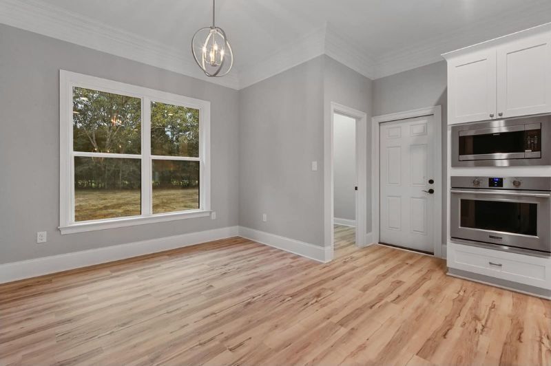 Empty kitchen with gray walls, wood floors, and white cabinets with built-in ovens.