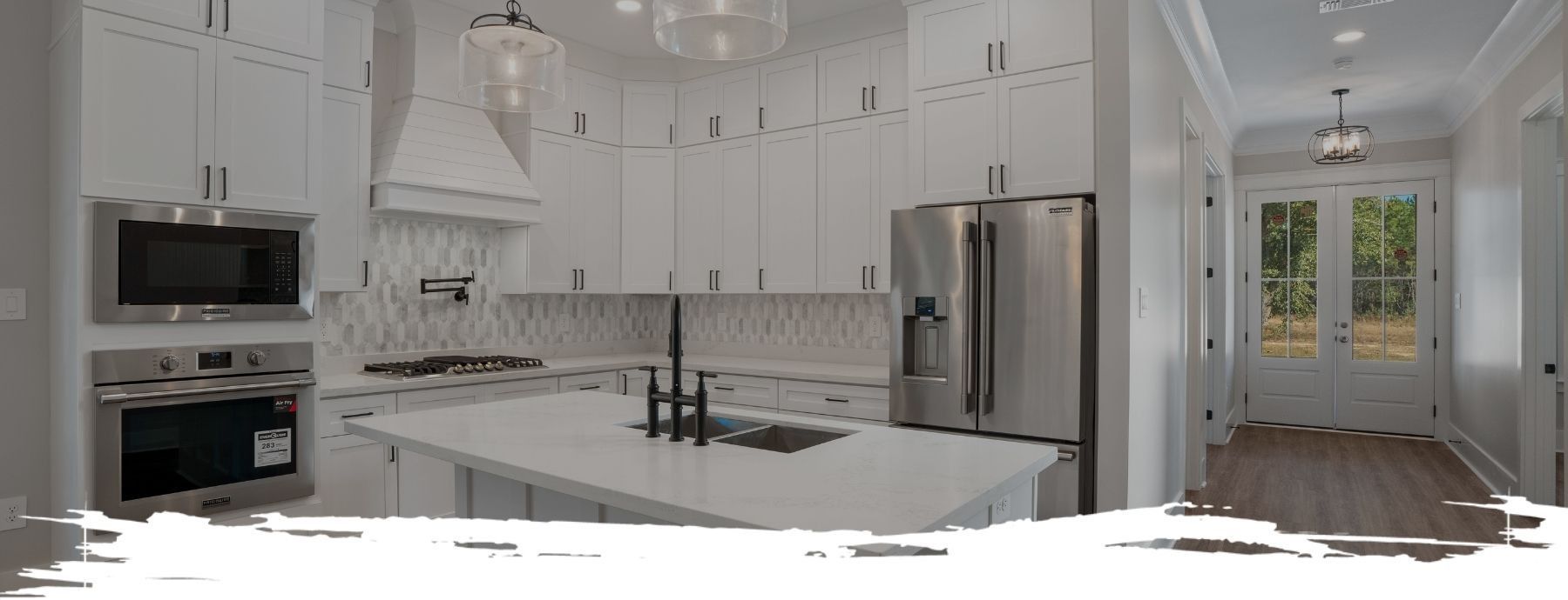 Modern white kitchen with stainless steel appliances, island and black accents, leading to an outdoor door.