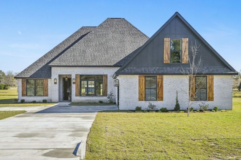 Brick home with gray roof, black gable, and wooden shutters on a green lawn.