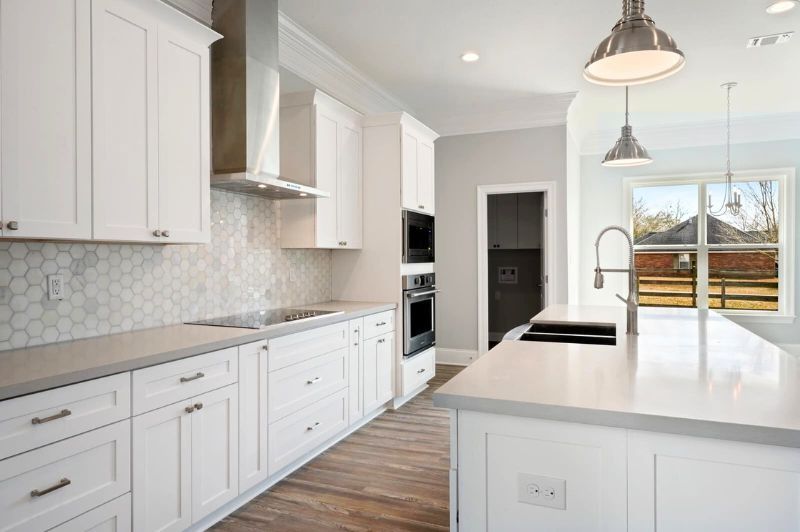 White kitchen with stainless steel appliances, white cabinets, light countertops, and gray walls.