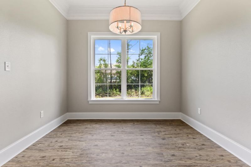 Empty room with a window. Beige walls, light wooden floor, white trim and a chandelier.
