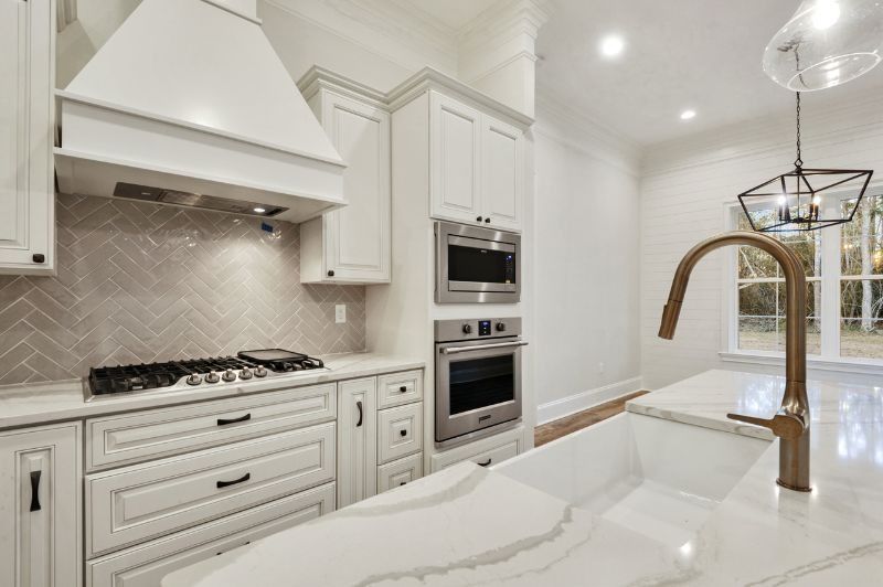 White kitchen with marble countertops, oven, microwave, and bronze faucet.