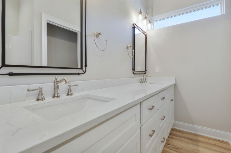 Bathroom vanity with white countertop, sinks, mirrors, and cabinetry. Light gray walls and pale wood flooring.