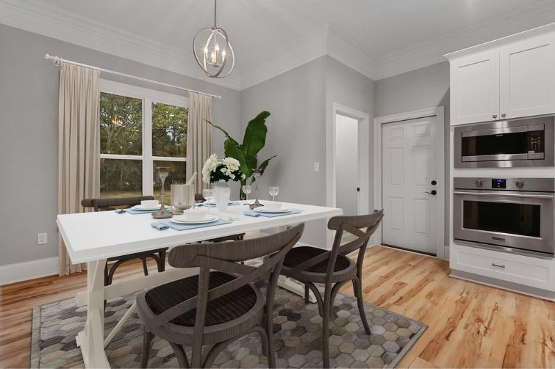 A modern dining room with a white table, gray chairs, and a window with light gray walls and wood floors.