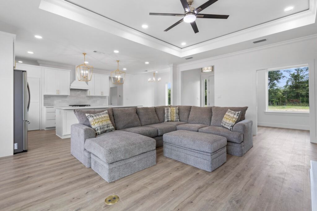 Spacious, bright living room with gray sectional sofa, open kitchen, and large window.