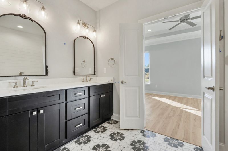 Bathroom with black vanity, floral tile floor, and arched mirrors. Doorway leads to a bedroom.