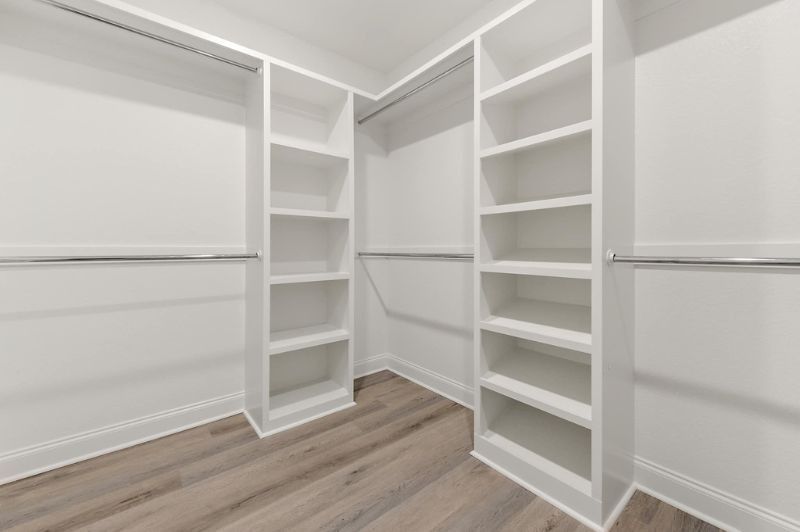 White closet with shelves and rods, featuring light wood flooring.