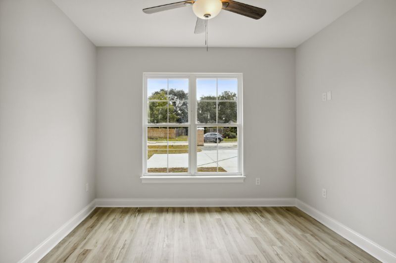 Empty room with light gray walls, a window, and wood-look flooring. A ceiling fan hangs overhead.