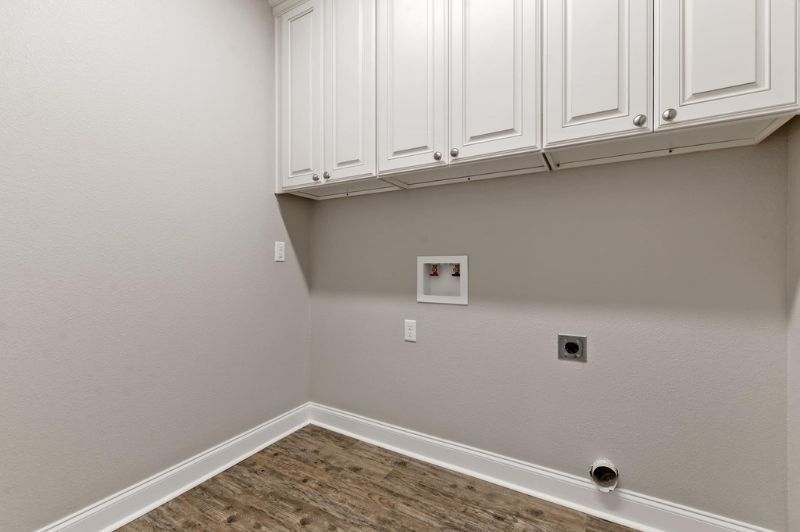 Laundry room with white cabinets, beige walls, and wood-look floor. Washer/dryer hookups on the wall.